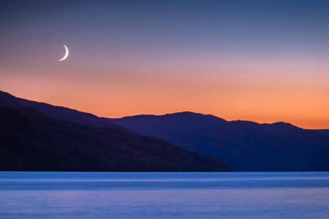 A waxing crescent moon sitting above the orange glow of sunset, Loch Sunart and the hills of Morvern | Sunart Scotland