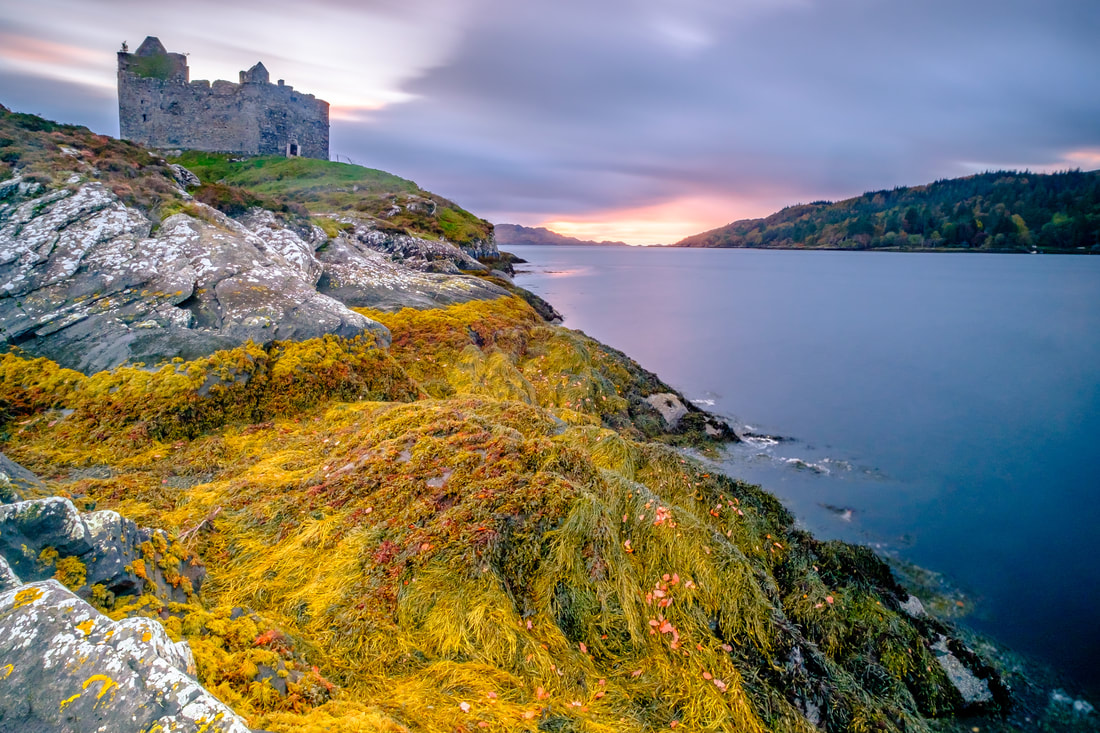 Castle Tioram standing guard over the southern entrance of Loch Moidart with the orange and pink glow from the setting sun on the horizon | Moidart Scotland
