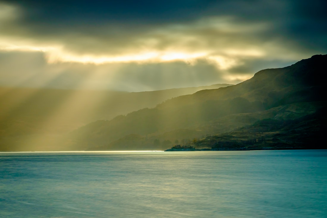 Crepuscular rays of sunlight breaking through the clouds and bathing the hills of Morvern and Loch Sunart in golden light | Sunart Scotland