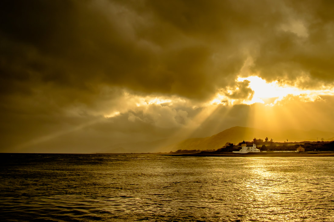 Crepuscular rays, or sunbeams, breaking through the clouds above Corran Lighthouse to create a golden scene | Ardgour Scotland