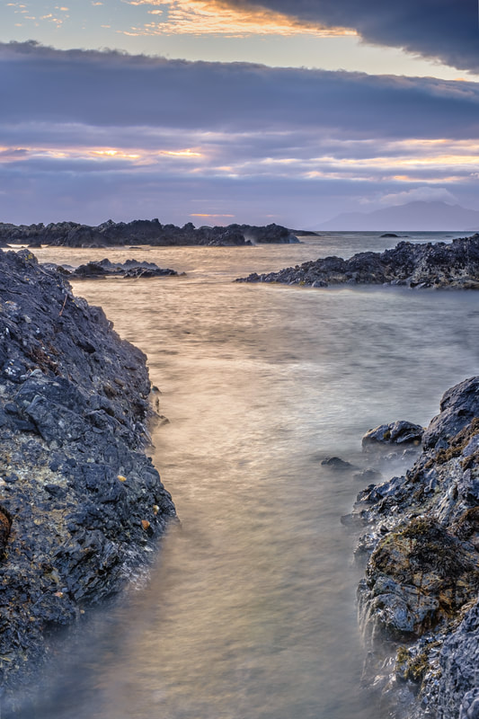High tide at sundown out on the rocks around Kilmory Beach with waves surging into a rock channel and the Small Isles on the horizon | Ardnamurchan Scotland