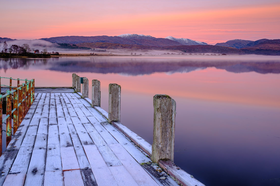 Frost covered jetty at Acharacle leading out into mirror-like Loch Shiel under mist and a pink sky of sunset | Ardnamurchan Scotland