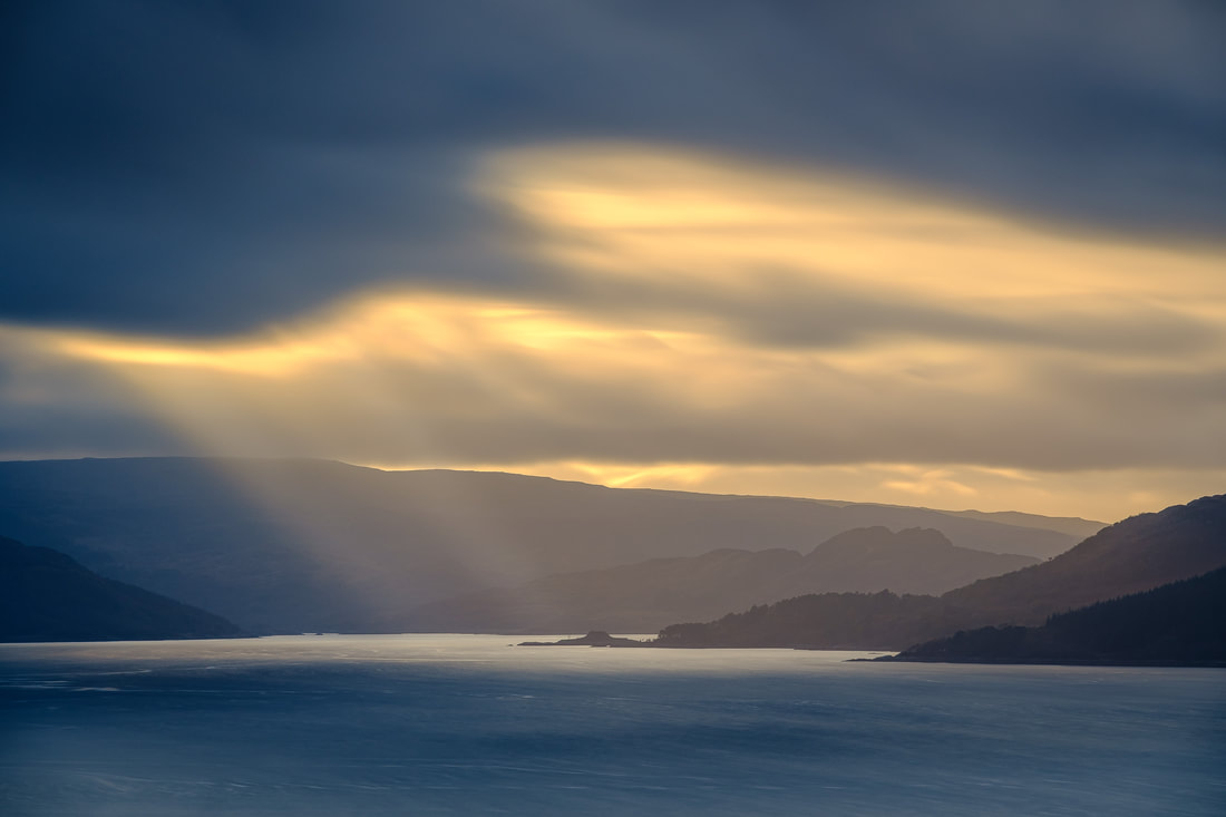 Crepuscular rays of afternoon sunlight breaking through the clouds over the western end of Loch Sunart and lighting up Dùn Ghallain | Sunart Scotland