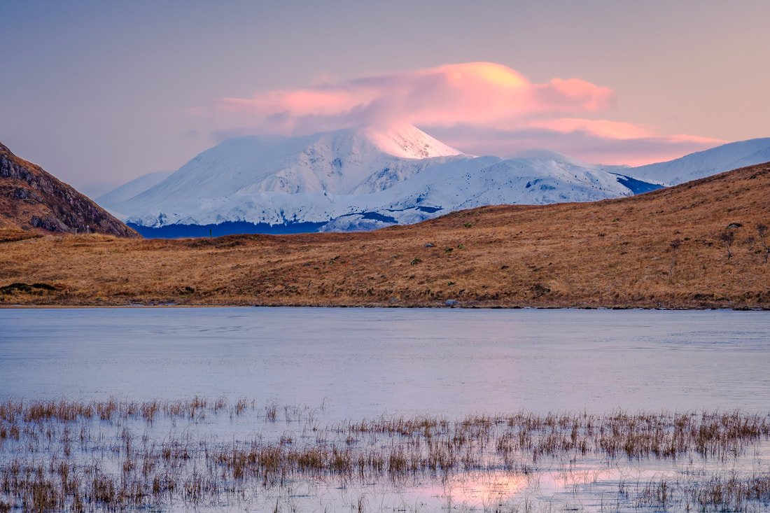 First light of a winter morning hitting a snow-covered Ben Nevis with its peak capped with cloud viewed from Lochan Doire a' Bhraghaid | Ardgour Scotland | Steven Marshall Photography