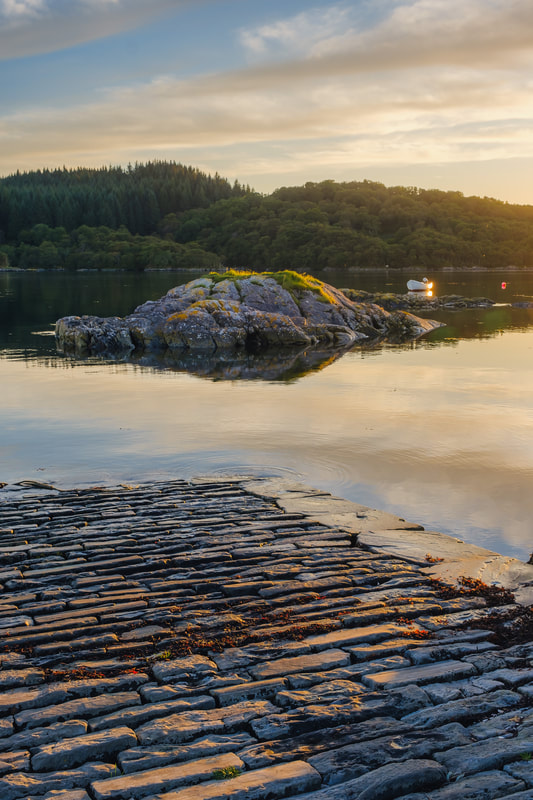 The old stone Ardtoe pier at the entrance to Kentra Bay warmly lit during the golden hour as sunset approaches | Ardnamurchan Scotland | Steven Marshall Photography
