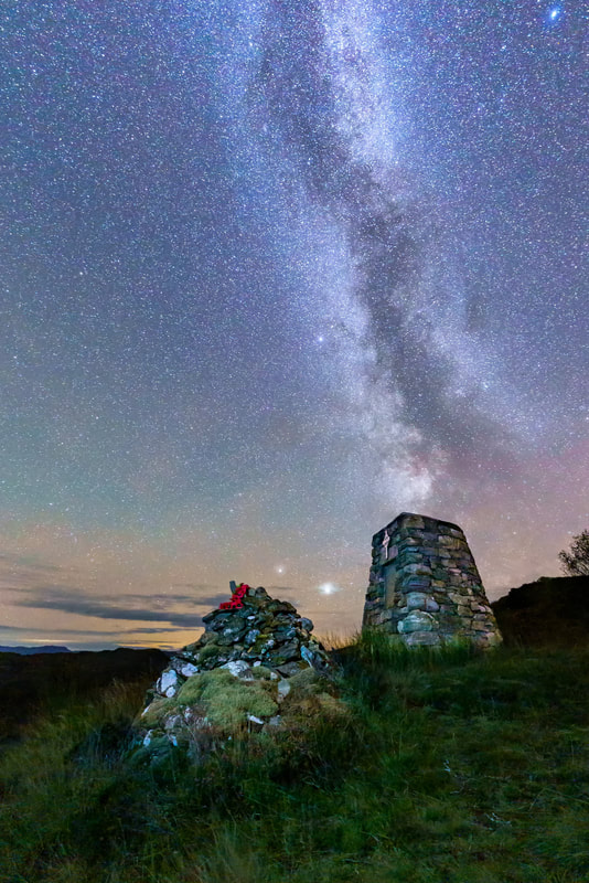 The Men and Women of Moidart War Memorial sitting under the Milky Way and behind a stone coffin cairn at the top Bealach Carach, Glenuig | Moidart Scotland