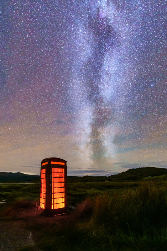The solitary phone box at the Newton junction on the road to Ardtoe illuminated with a red light while the Milky Way soars above it and the salt marsh around Kentra Bay | Ardnamurchan Scotland