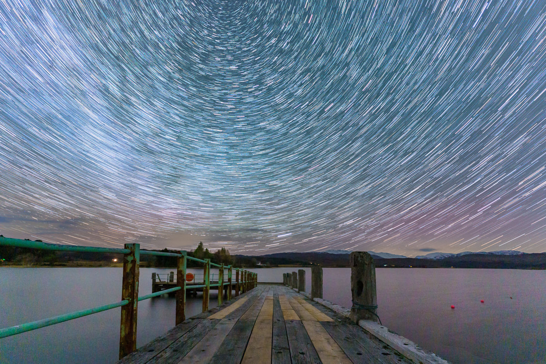 A fifteen-minute startrail of the night sky rotating above the jetty in Acharacle that leads north out into Loch Shiel | Ardnamurchan Scotland