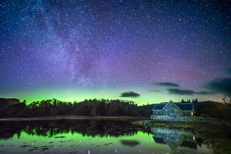 The still waters of Loch Aline, lit up green by the Northern Lights up in the sky beyond the old boathouse at Ardtornish Estate.