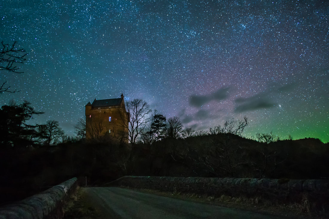 Kinlochaline Castle sitting under a starry sky by the bridge over the River Aline while Northern Lights illuminate the sky to the north | Morvern Scotland
