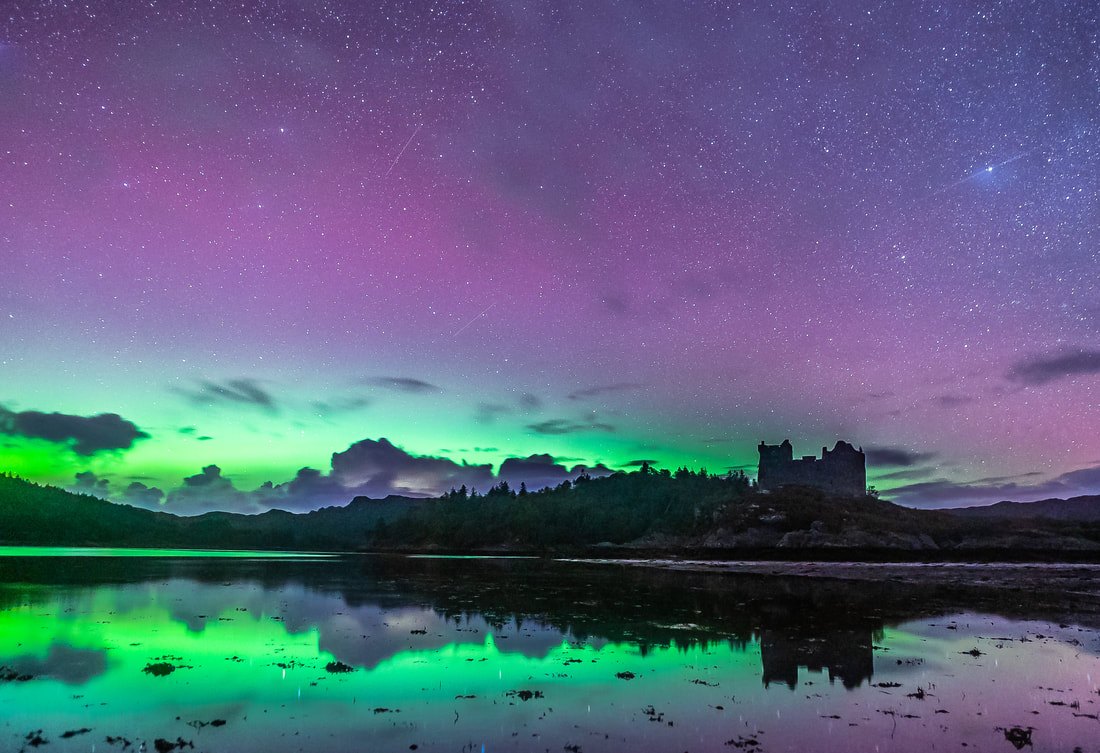 The sky above Castle Tioram and the sea below it lit up with greens and purples from the Northern Lights | Moidart Scotland