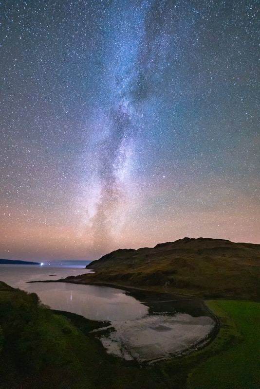 The pink-red tinge of Airglow emanating from the western beyond the bay of Camas Nan Geall with the Milky Way rising up into the sky above it | Ardnamurchan Scotland